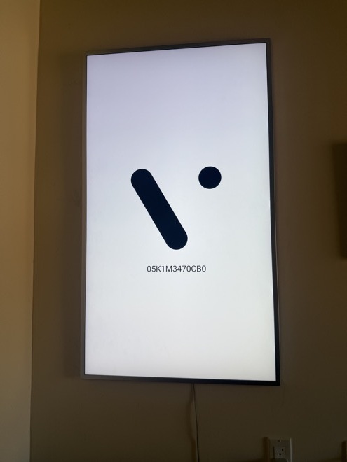 A wall-mounted screen showing a white background with its serial number